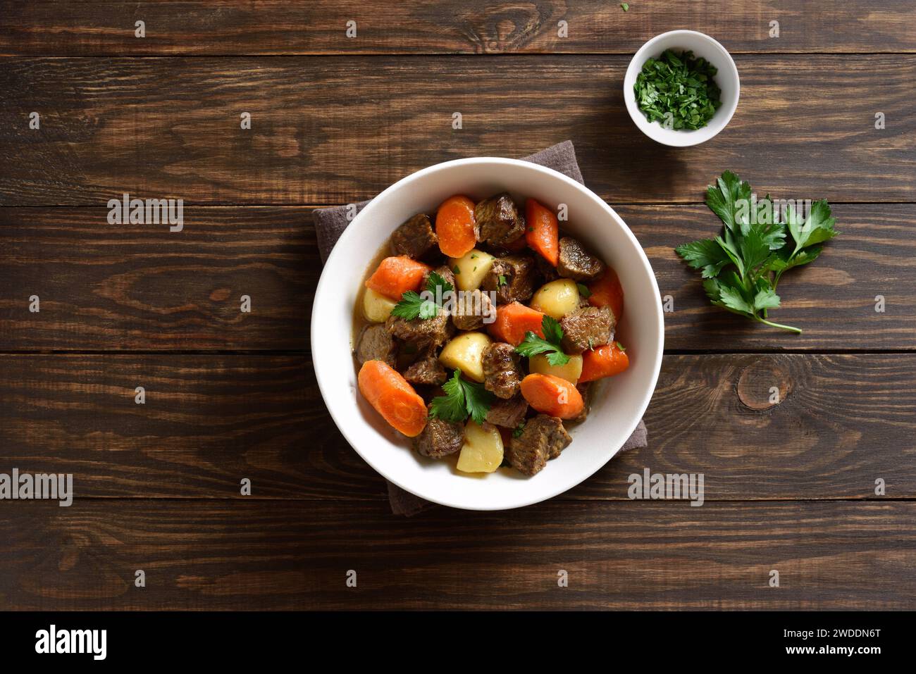 Beef meat stewed with potatoes, carrots and spices in white bowl over wooden background. Comfort healthy food for dinner. Top view, flat lay Stock Photo