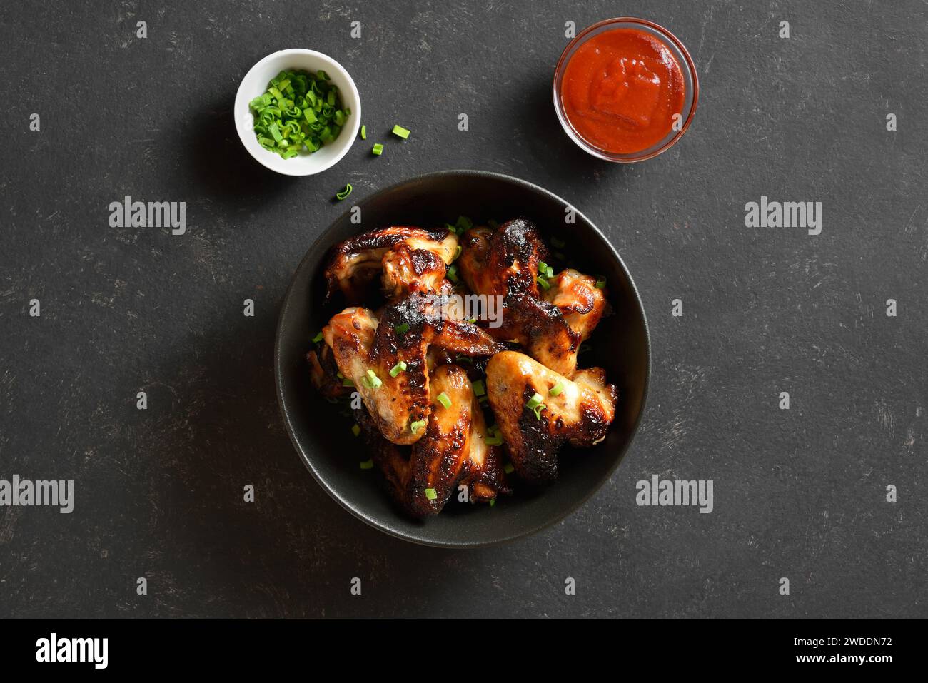 Grilled chicken wings in bowl over dark stone background. Tasty bbq chicken for dinner. Top view, flat lay Stock Photo