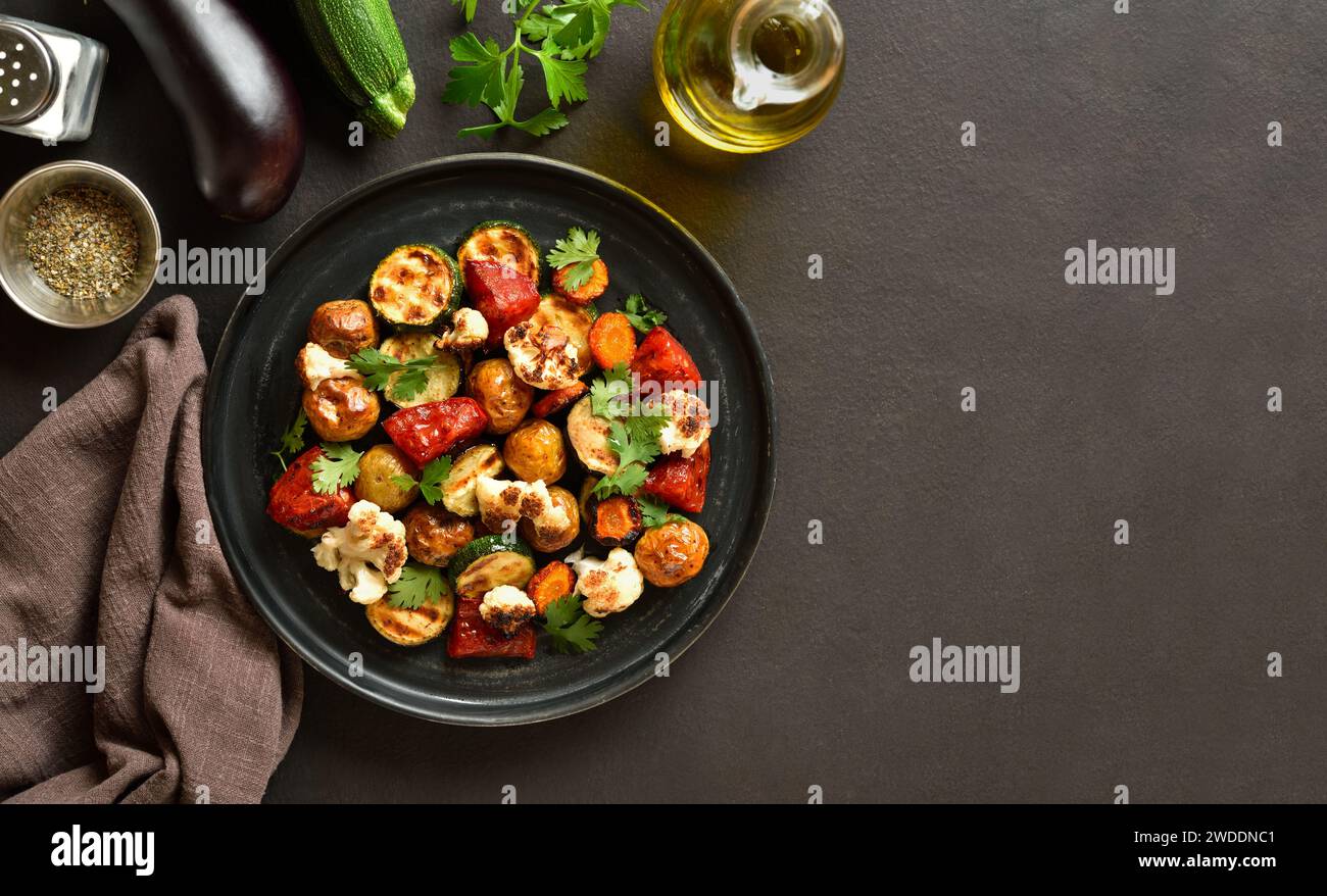 Roasted vegetables on plate over dark background with copy space. Tasty mix oven baked vegetables for dinner. Top view, flat lay Stock Photo