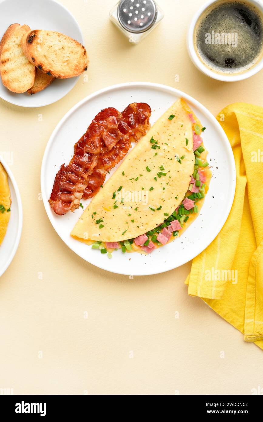 Stuffed omelette with ham and green onion on plate over light background. Tasty healthy meal for breakfast. Top view, flat lay. Stock Photo