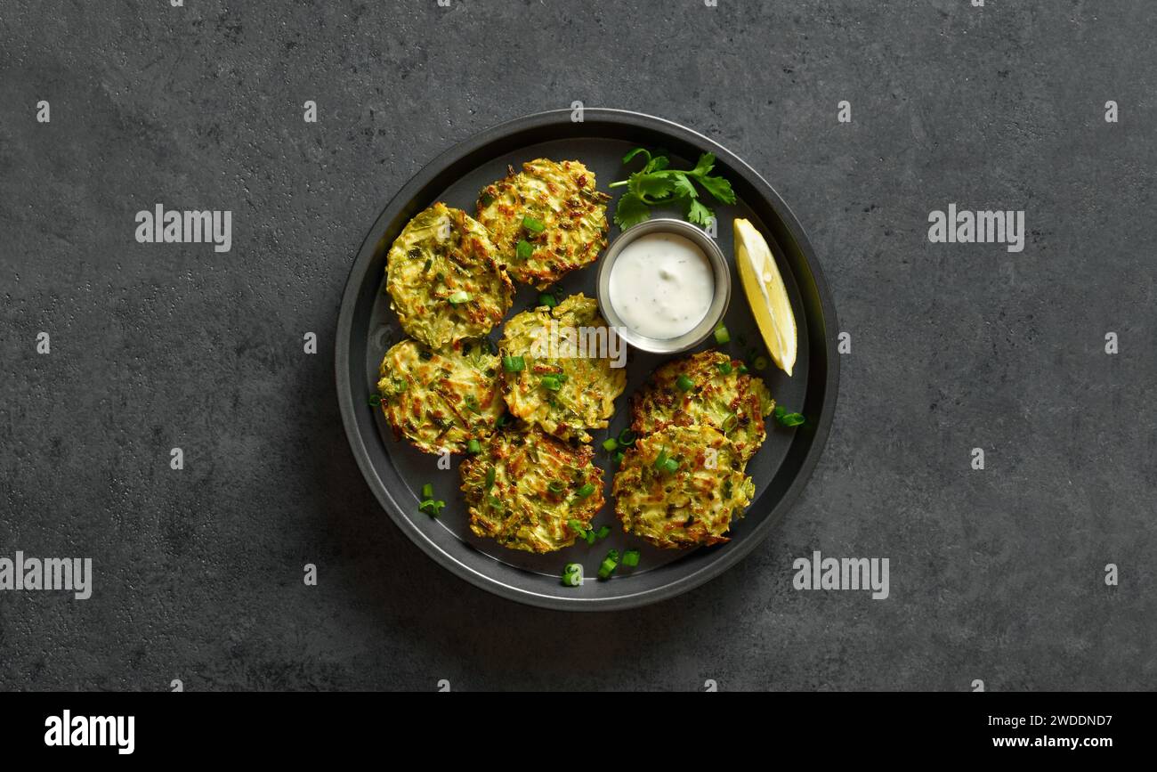 Vegetable vegetarian zucchini fritters served with sauce on plate over dark stone background with copy space. Top view, flat lay Stock Photo