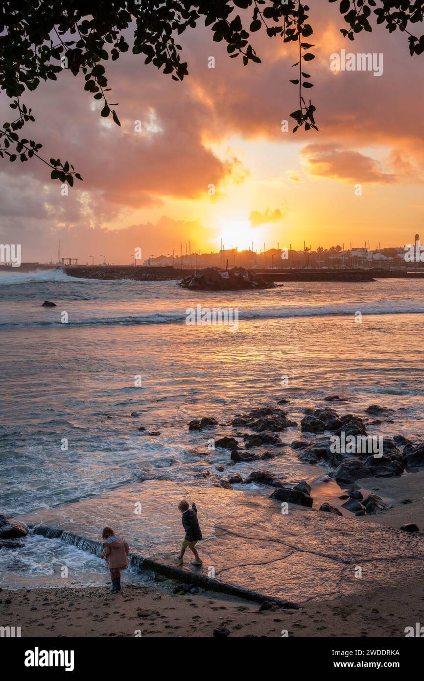 Two children playing by the harbour at Saint-Pierre, Terre-Sainte, Reunion Island, at sunset. The tropical island is a popular travel destination. Stock Photo