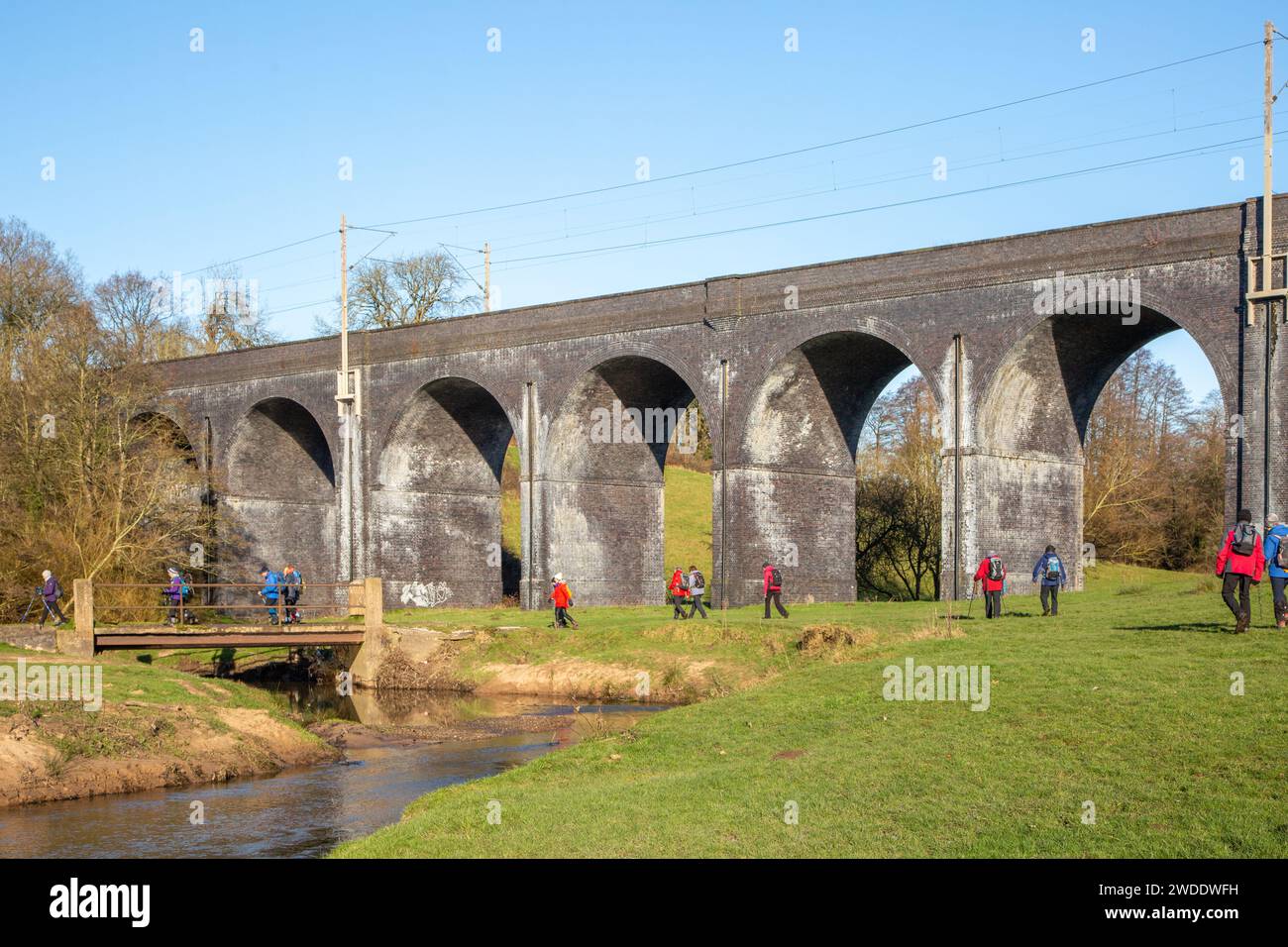 Walking group of ramblers in the Cheshire countryside walking along the river Dean approaching the  railway Viaduct  near Wilmslow Cheshire Stock Photo