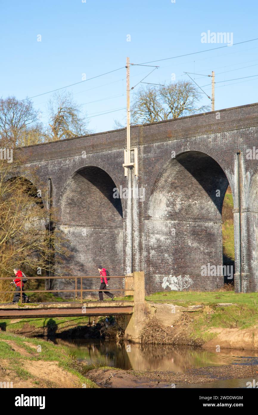 Ramblers walking in the Cheshire countryside walking over  a bridge crossing the river Dean at the foot of the  railway Viaduct at Wilmslow Cheshire Stock Photo