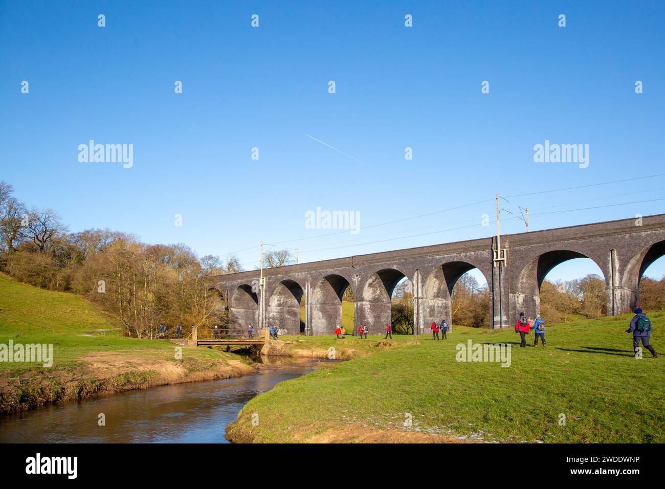 Walking group of ramblers in the Cheshire countryside walking along the river Dean approaching the  railway Viaduct  near Wilmslow Cheshire Stock Photo