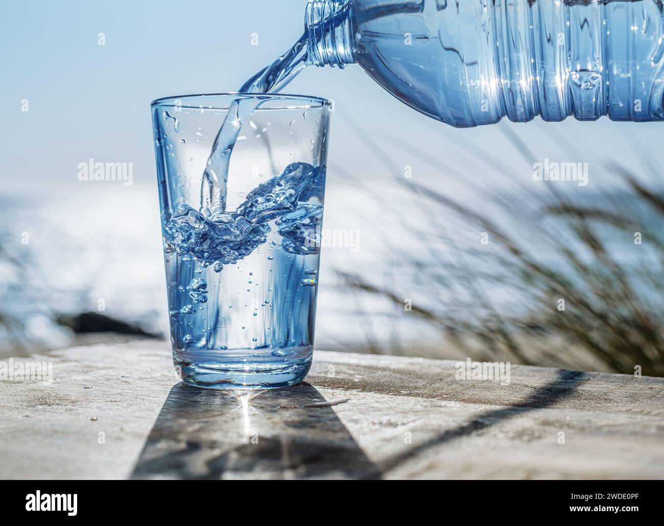 Pouring water into a glass from plastic bottle. Nature background. Stock Photo