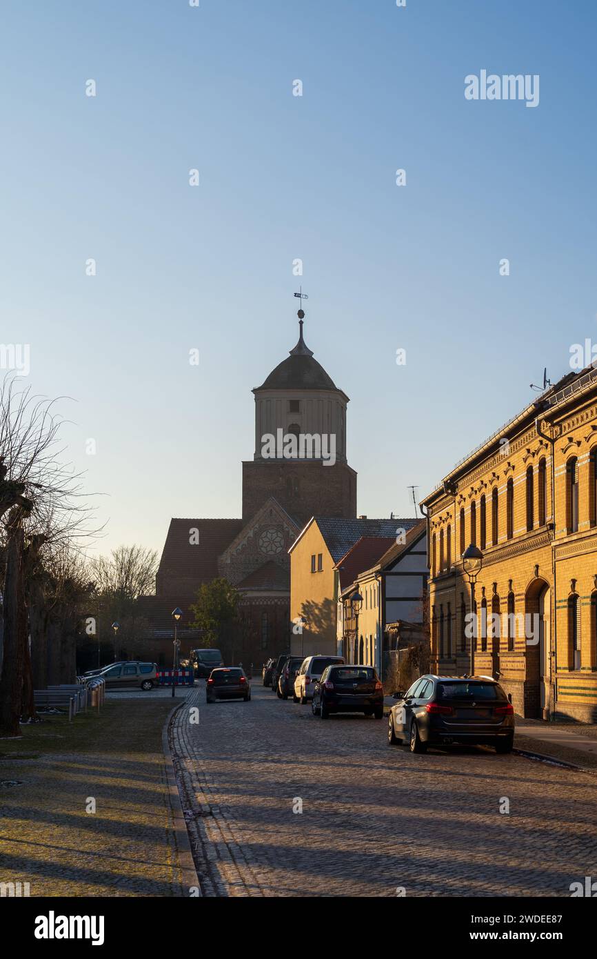 A serene evening view of a cobblestone street in Treuenbrietzen, with historic buildings and a church under the golden sunset. Stock Photo