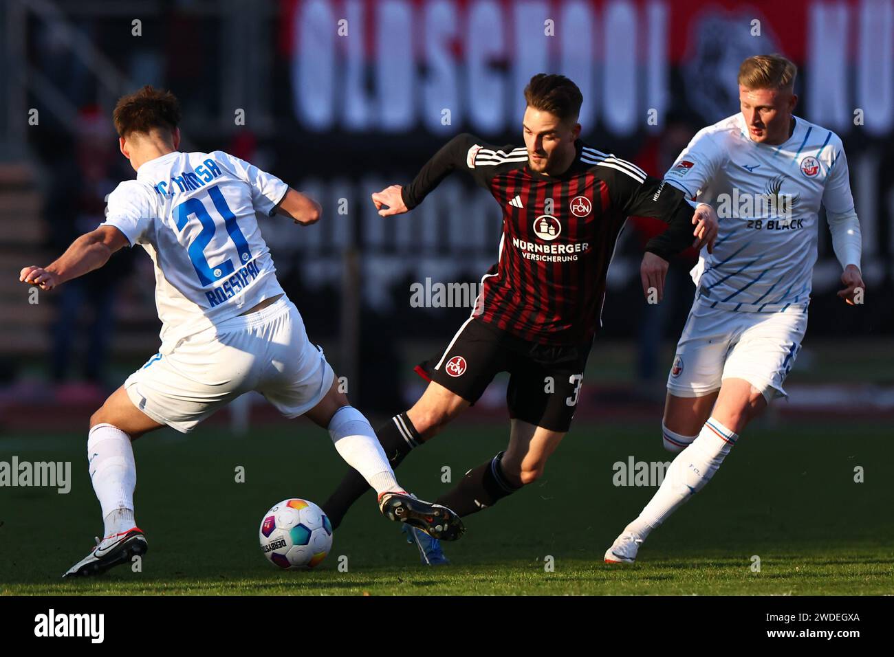 Nuremberg, Germany. 20th Jan, 2024. Soccer: Bundesliga 2, 1. FC Nuremberg - Hansa Rostock, matchday 18 at the Max Morlock Stadium. Nuremberg's Lukas Schleimer (center) battles for the ball with Hansa Rostock's Alexander Rossipal (left). Credit: Daniel Karmann/dpa - IMPORTANT NOTE: In accordance with the regulations of the DFL German Football League and the DFB German Football Association, it is prohibited to utilize or have utilized photographs taken in the stadium and/or of the match in the form of sequential images and/or video-like photo series./dpa/Alamy Live News Stock Photo