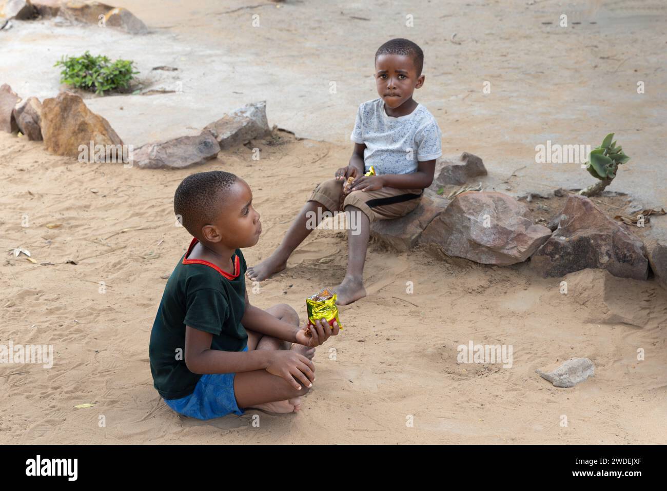 african children hanging in front of the house eating snacks and biscuits ,waiting for her mother Stock Photo