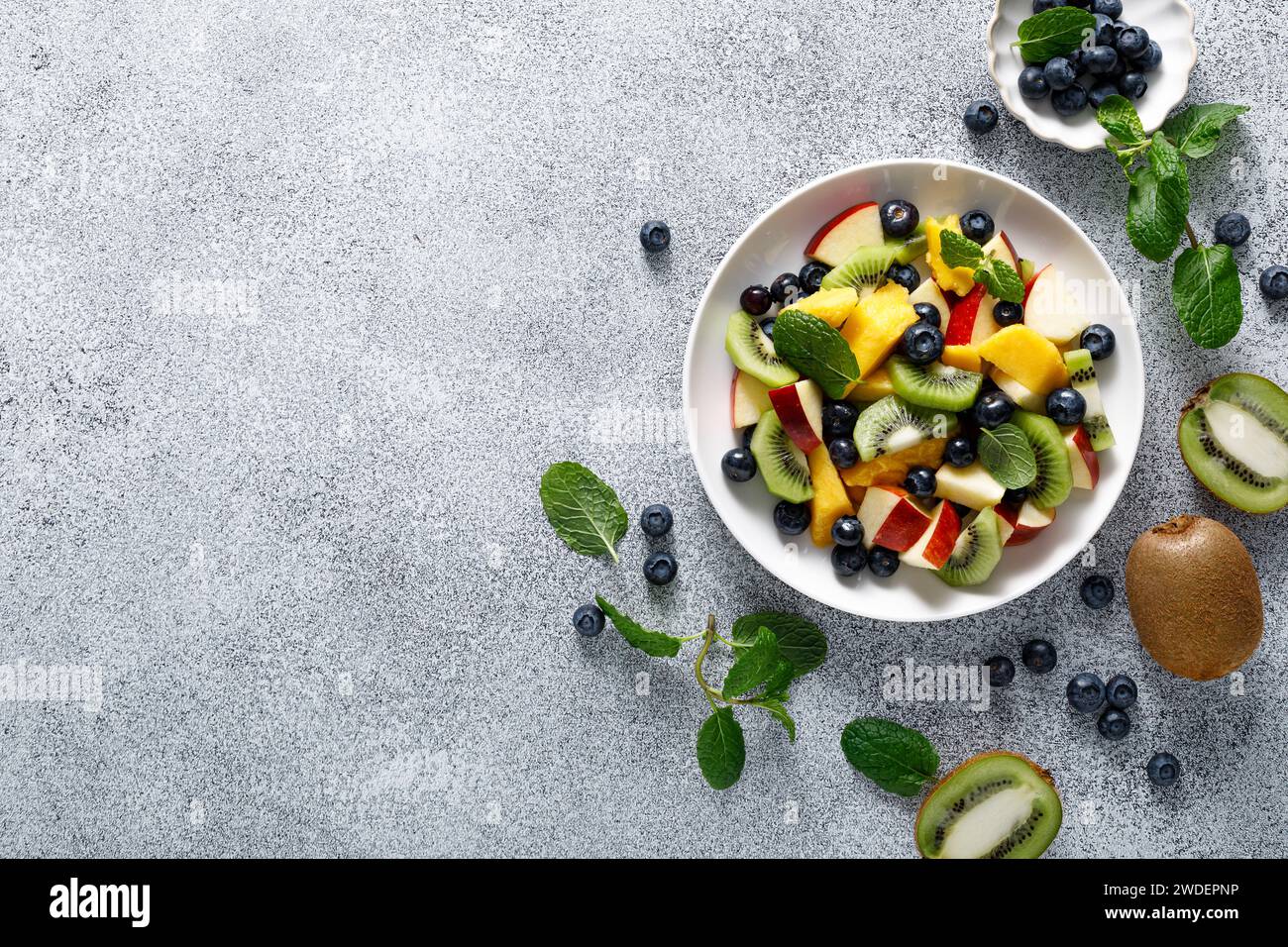 Fruit and berry salad with mango, kiwi, apple, blueberry and fresh mint leaves. Healthy food, diet. Top view Stock Photo