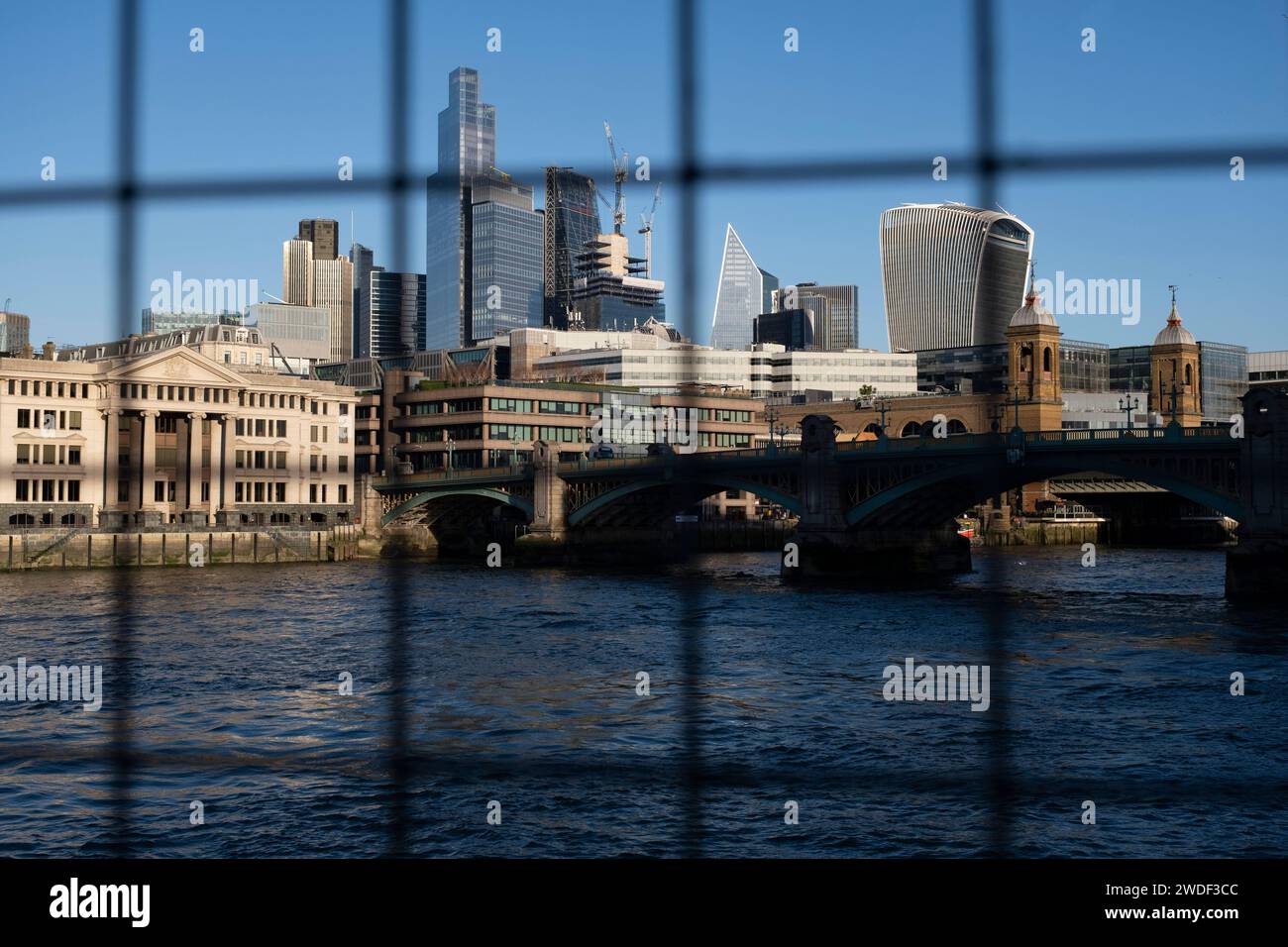 City of London skyline looking over the River Thames from behind metal mesh on 16th January 2024 in London, United Kingdom. The City of London is a city, ceremonial county and local government district that contains the primary central business district CBD of London. The City of London is widely referred to simply as the City is also colloquially known as the Square Mile. Stock Photo