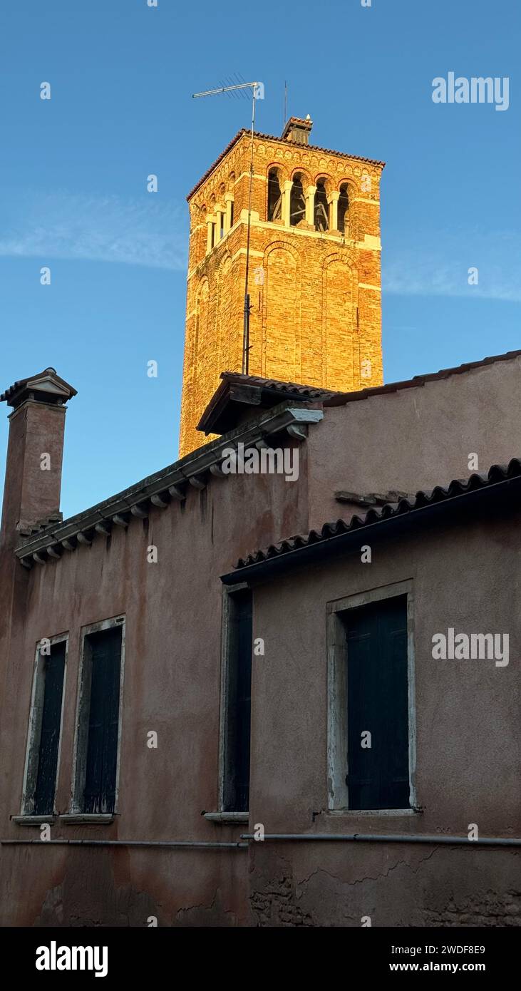 A majestic clock tower stands tall and proud, overlooking a charming brick building adorned with numerous windows Stock Photo