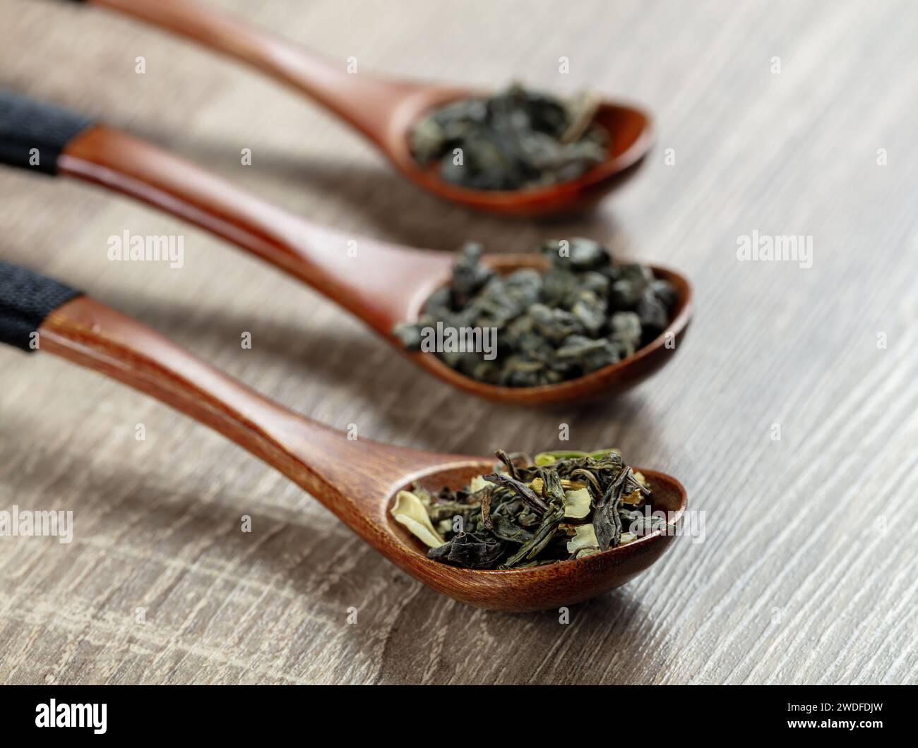 green tea leaves in a spoons on wooden background; dried Chinese green tea long leaves; small bunches Stock Photo
