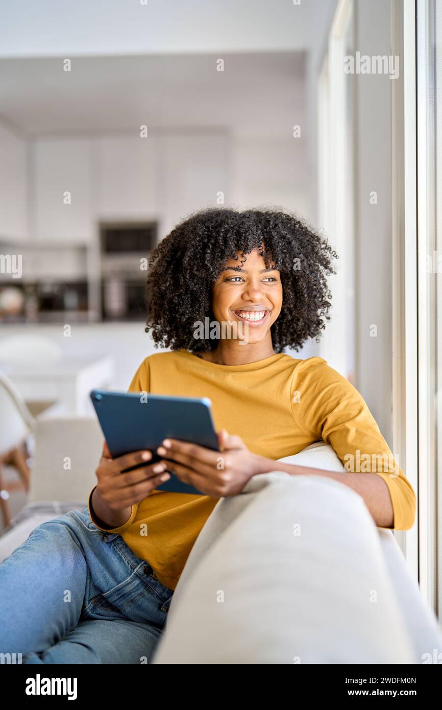 Happy young African American woman using tab looking away at home. Stock Photo