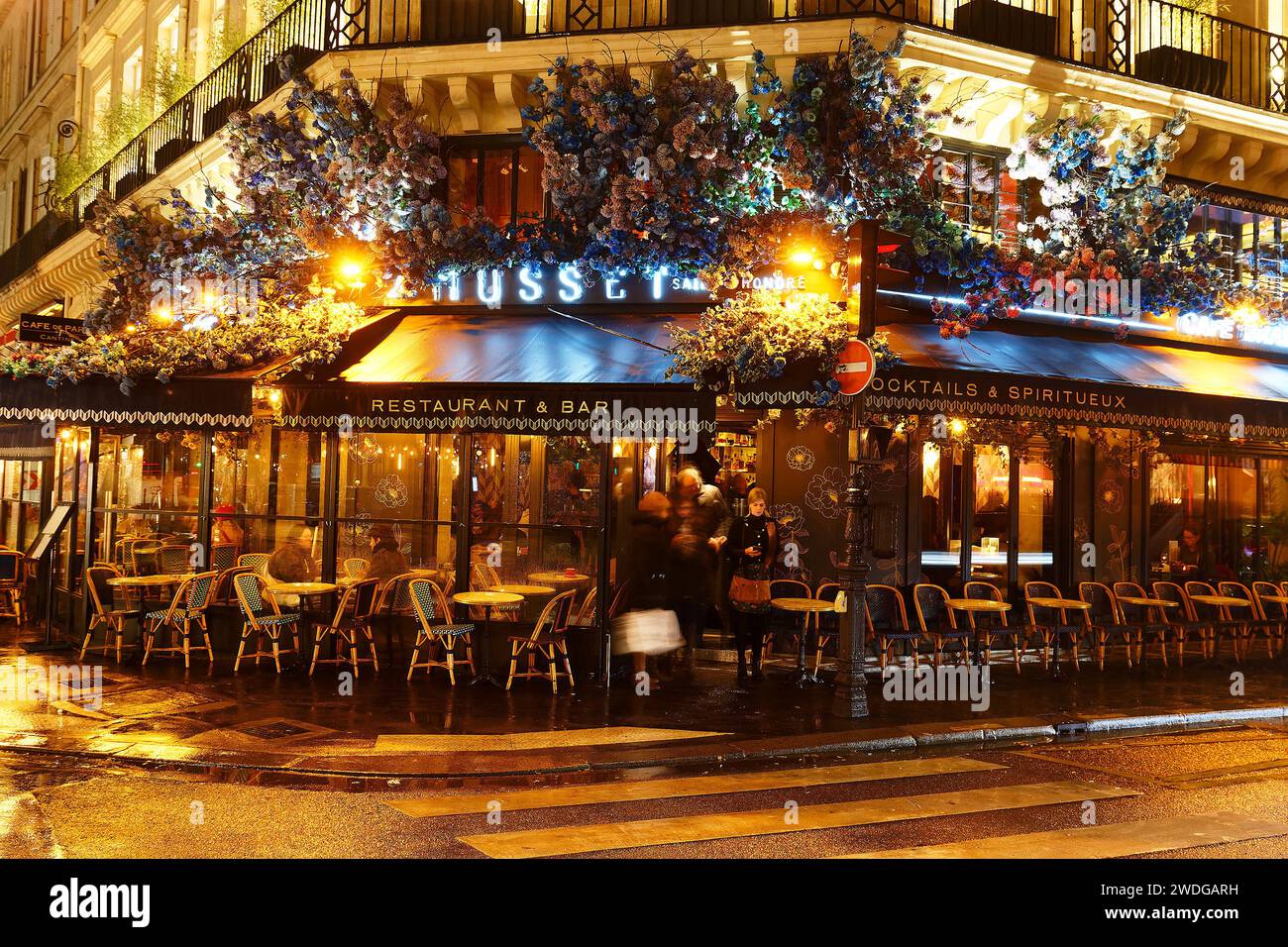 Exterior of Le Musset traditional French restaurant decorated with beautiful blue hydrangea flowers at rainy night. Paris. France. Stock Photo