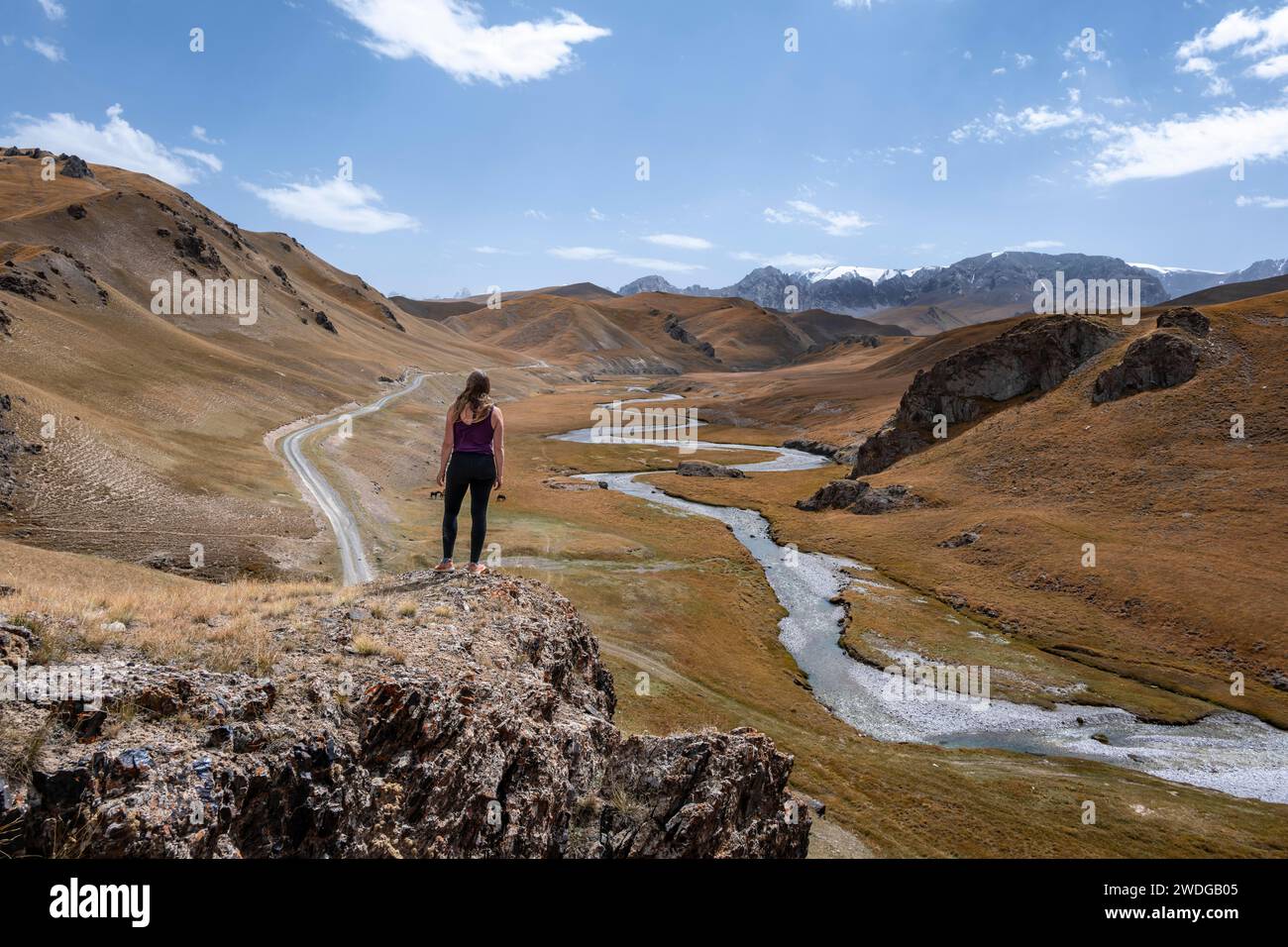 Tourist on a hill, Kol Suu river winds through a mountain valley with hills of yellow grass, Naryn province, Kyrgyzstan Stock Photo