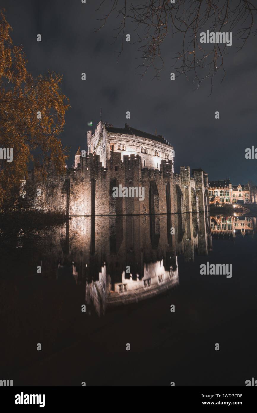Night portrait of the medieval Gravesteen Castle in the centre of Ghent, Belgium. The reflection of the walls is in the water channel. Stock Photo