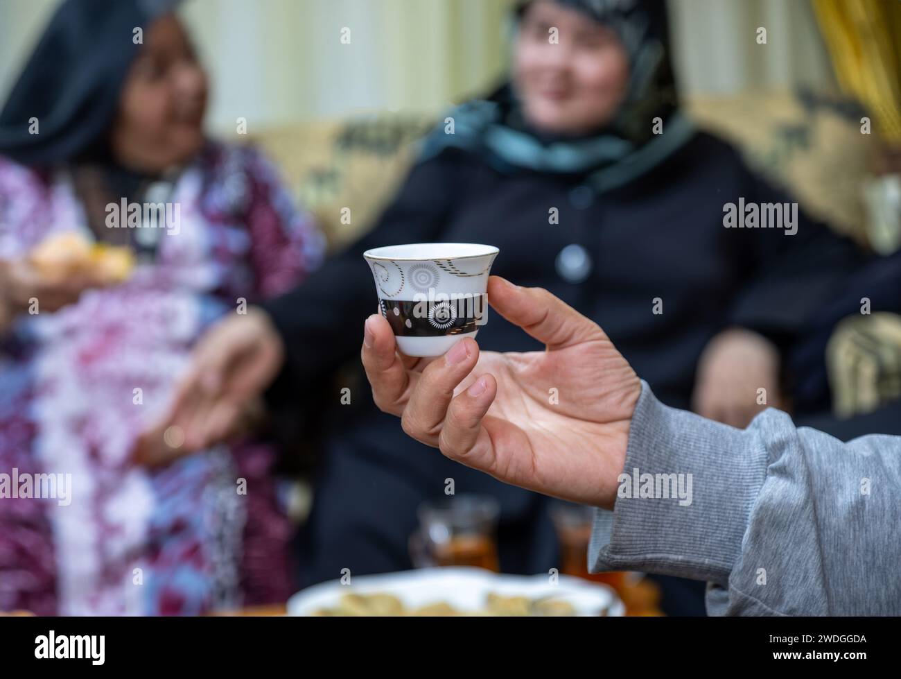 hand holding coffee cup with family in the background Stock Photo