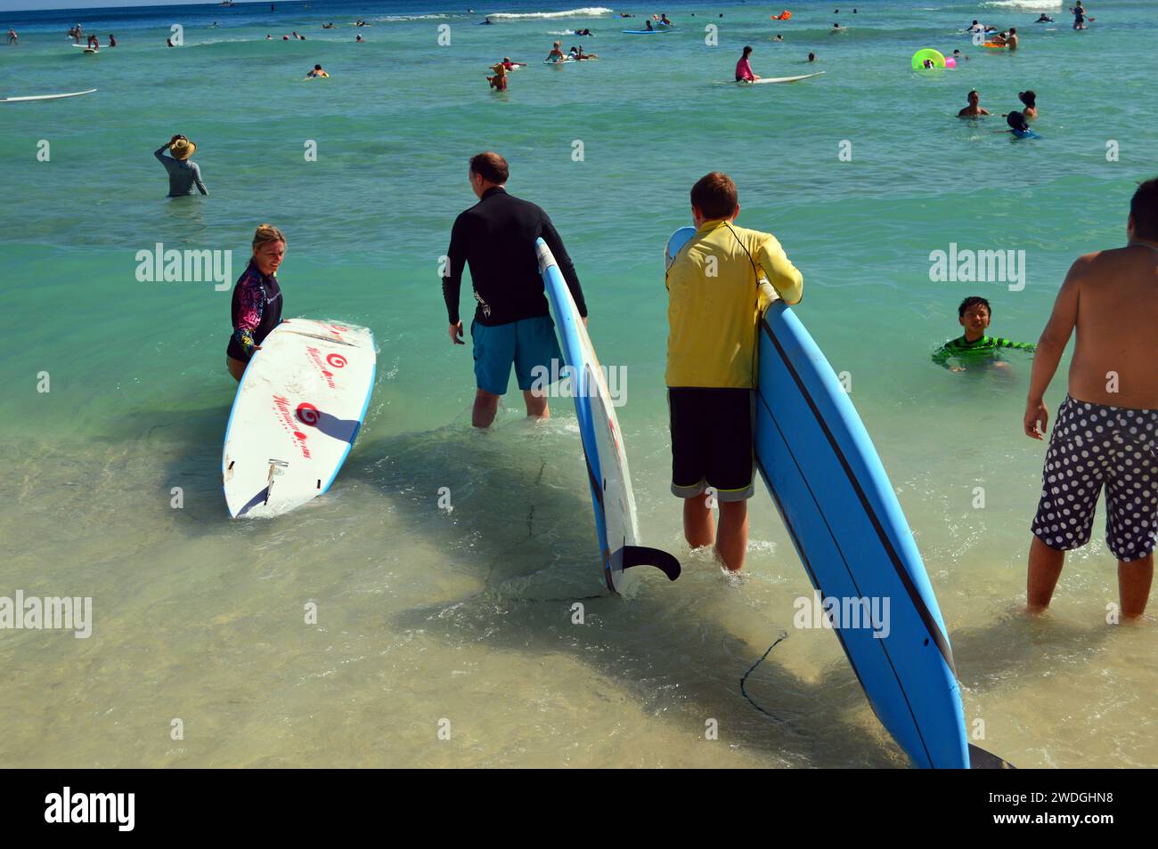 Surfers leave the beach and head into a crowded ocean for a surf lesson on a summer vacation day in Waikiki Beach Stock Photo