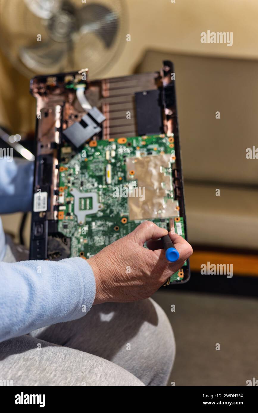 old woman with a laptop computer in her lap and screwdriver in her hand trying to repair it Stock Photo