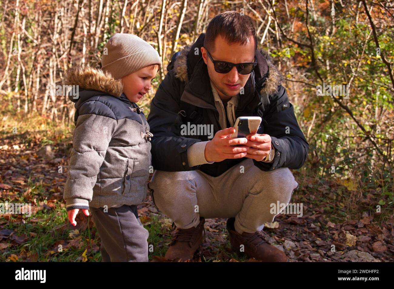 Father and his toddler using mobile phone in the forest Stock Photo