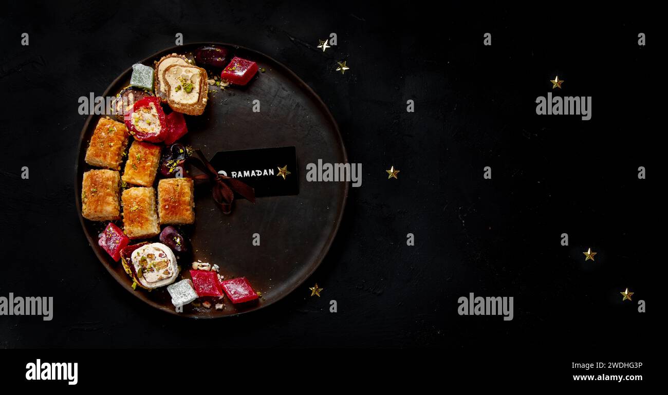 Ramadan food on a large plate. Arabic sweets - lokum, fruit marmalade, baklava on a black background. Top view, copy space Stock Photo