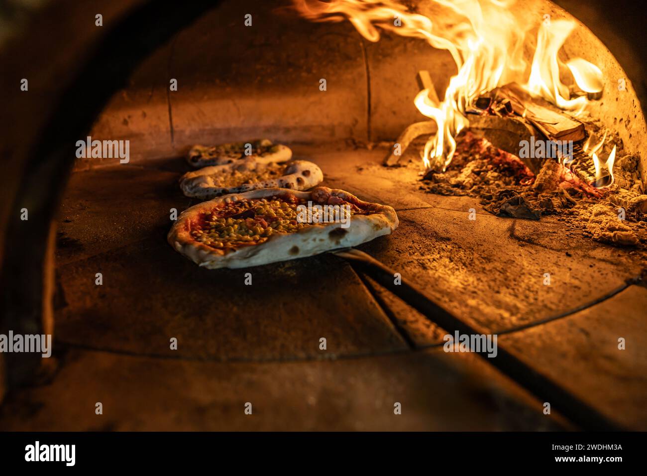 Traditional oven for baking pizza with burning wood and shovel. The cook rotates the pizza in the oven to ensure even baking. Stock Photo
