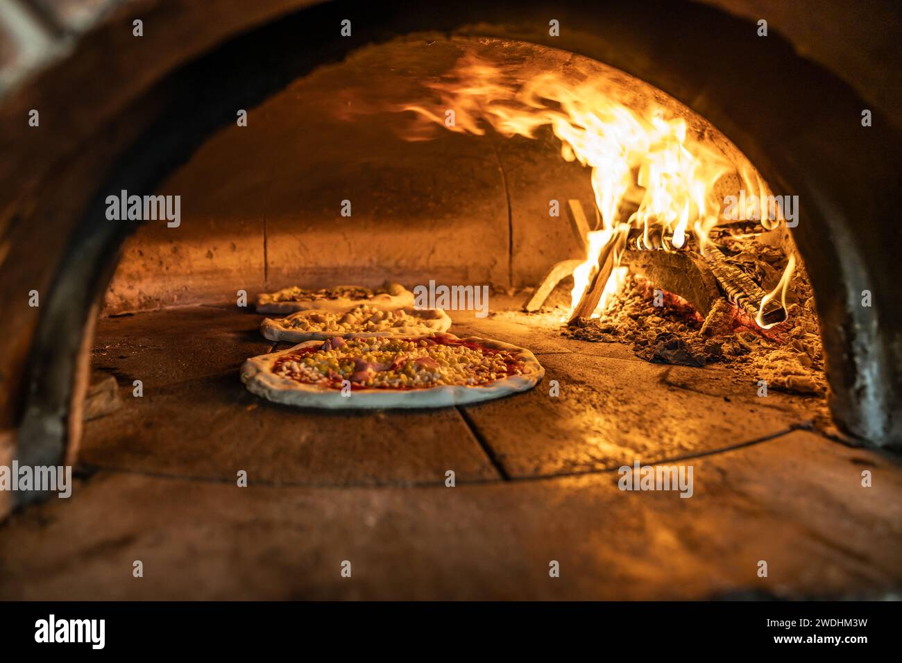 Traditional oven for baking pizza with burning wood and shovel. Several pizzas are baked in a brick oven. Stock Photo