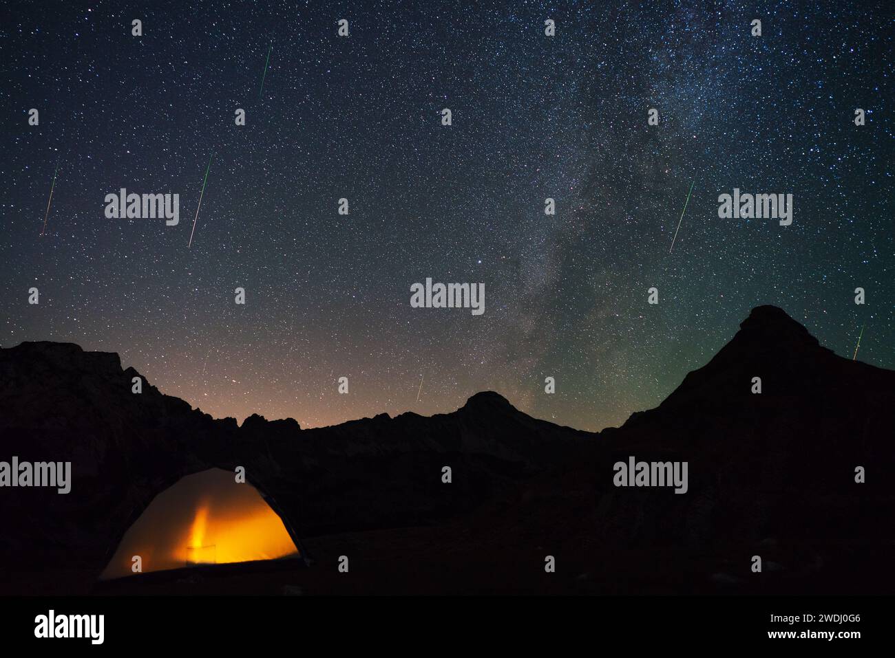 A view of a Meteor Shower and the Milky Way with tent and mountains silhouette in the foreground. Stock Photo