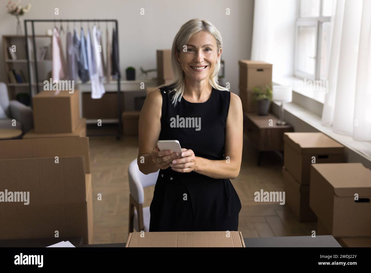 Attractive middle-aged woman holds cellphone ordering delivery courier services Stock Photo