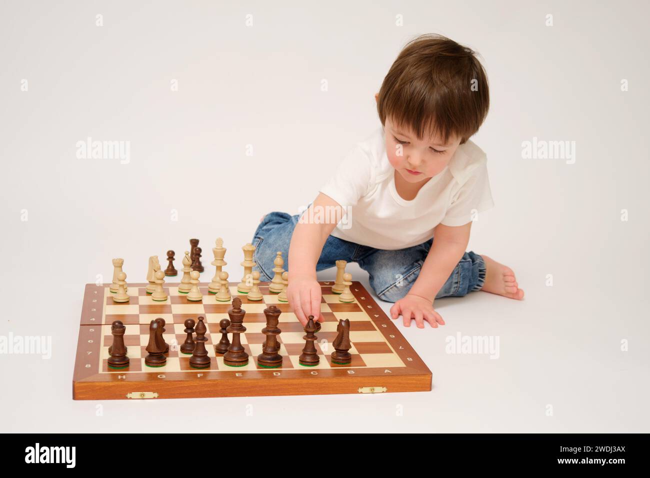 Toddler baby playing chess, studio white background. A child with chess pieces on a chessboard Stock Photo