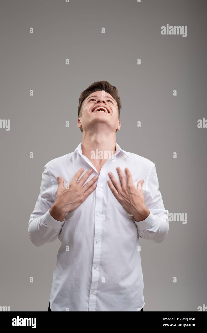 Overwhelmed with happiness, he clutches his chest in a white shirt