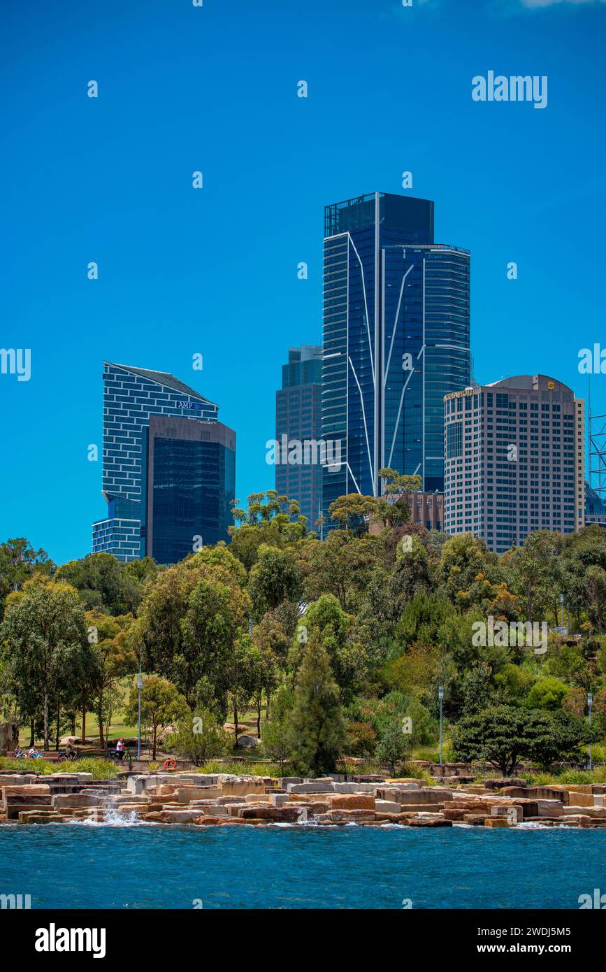 Looking over the sandstone shoreline and greenery of North Barangaroo Reserve to the modern city high rise buildings in Sydney, Australia Stock Photo
