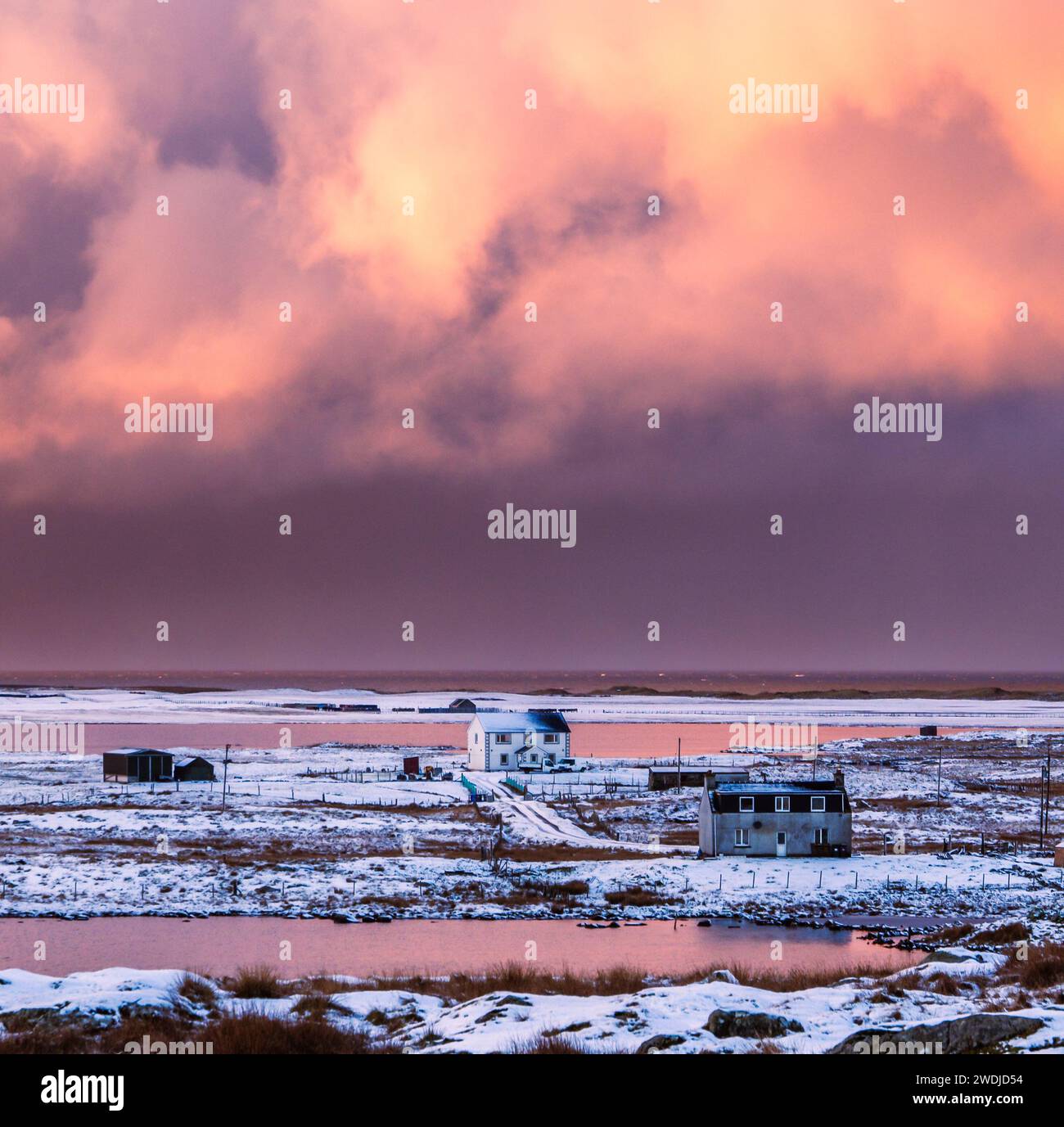 Pink reflections in the lochs by Township Croft houses of Bornish at Sunset during rare snow in South Uist 2024, Outer Hebrides, Scotland Stock Photo