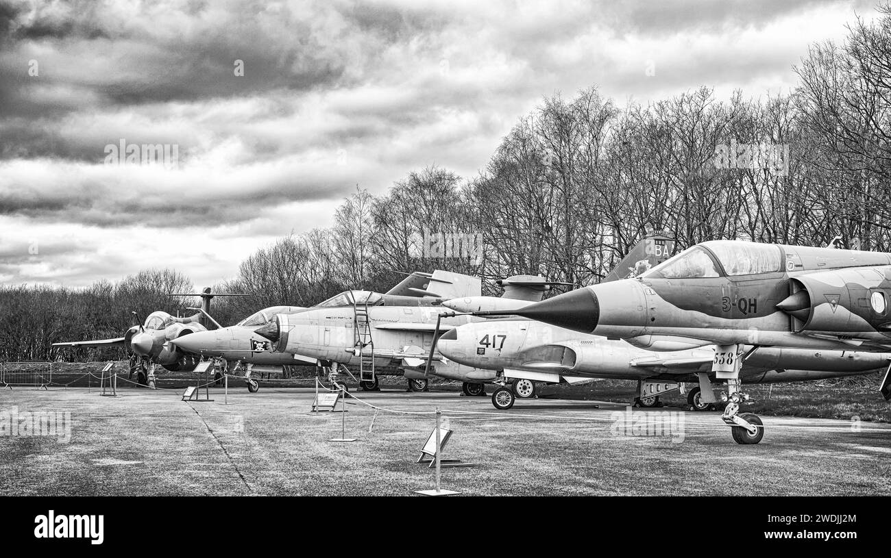 A line of aircraft including a Mirage, English Electric Lightening, with a Buccaneer at the far end. A line of trees is behind and a sky with cloud ab Stock Photo