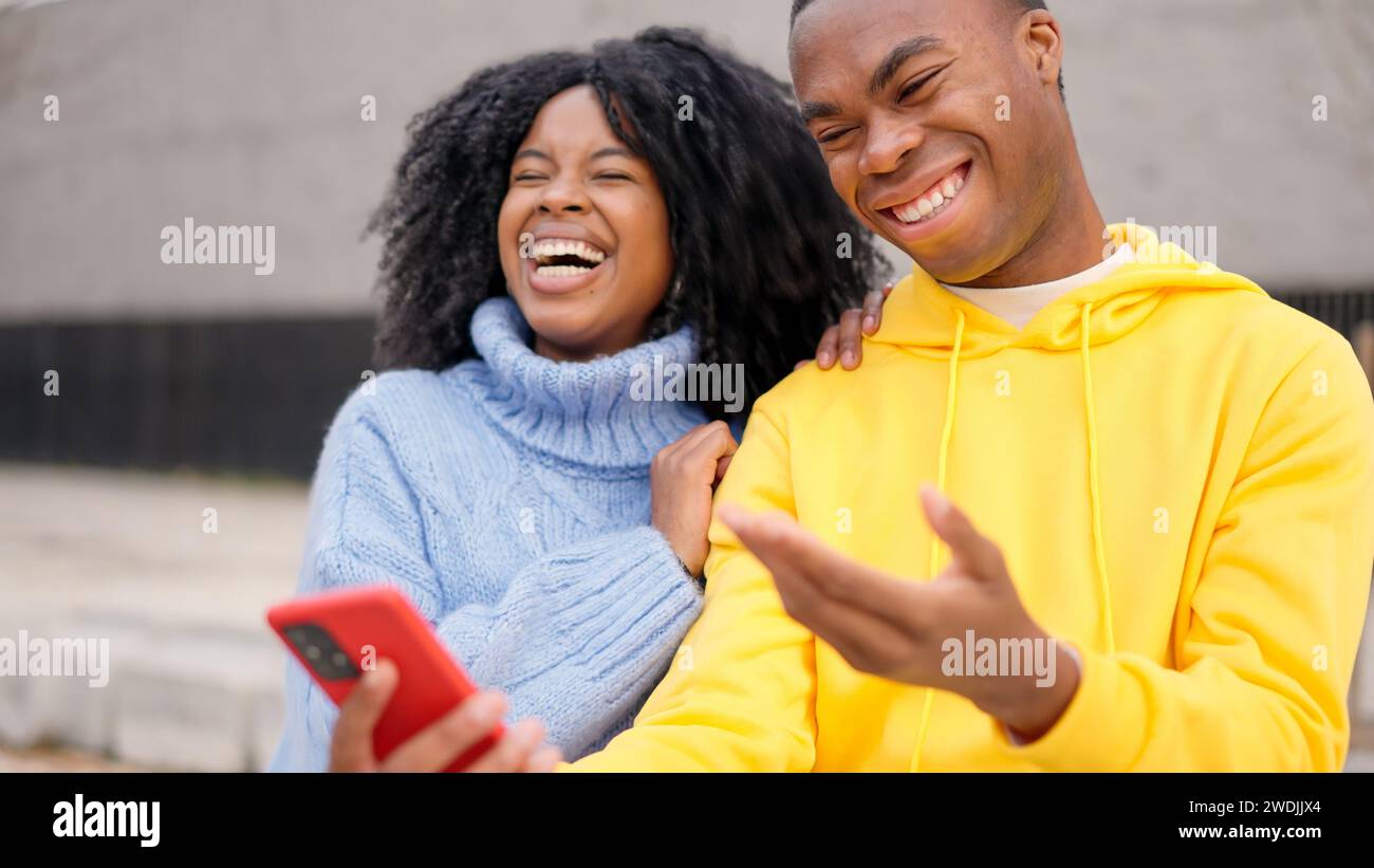 African couple having fun using mobile in the street Stock Photo