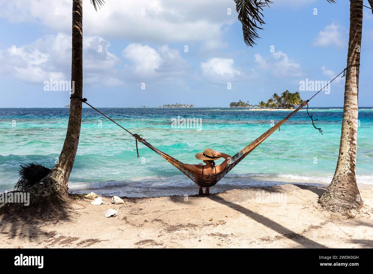 Woman tourist in a hammock with straw hat on her head relaxing on a idyllic tropical island in indigenous territory of Guna Yala in Panama Stock Photo