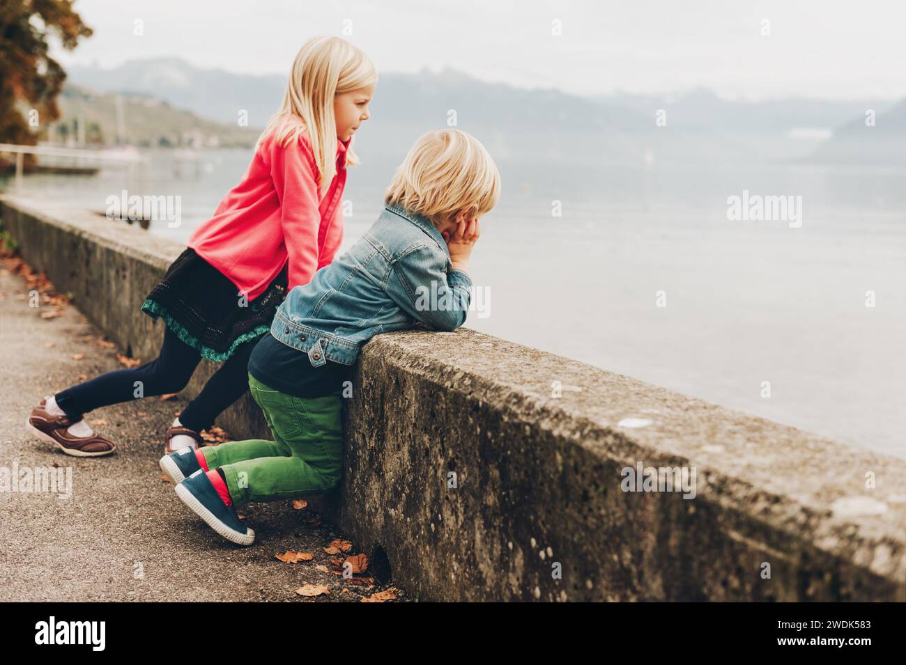 Two funny kids enjoying nice and warm autumn day next to lake Geneva. Little brother and big sister spending time together outside Stock Photo