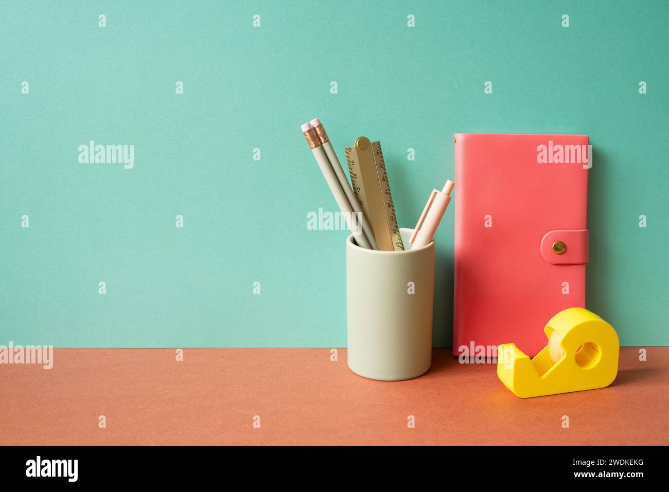 Pink diary notebook and writing supplies stationery in holder on red desk. mint green wall background Stock Photo