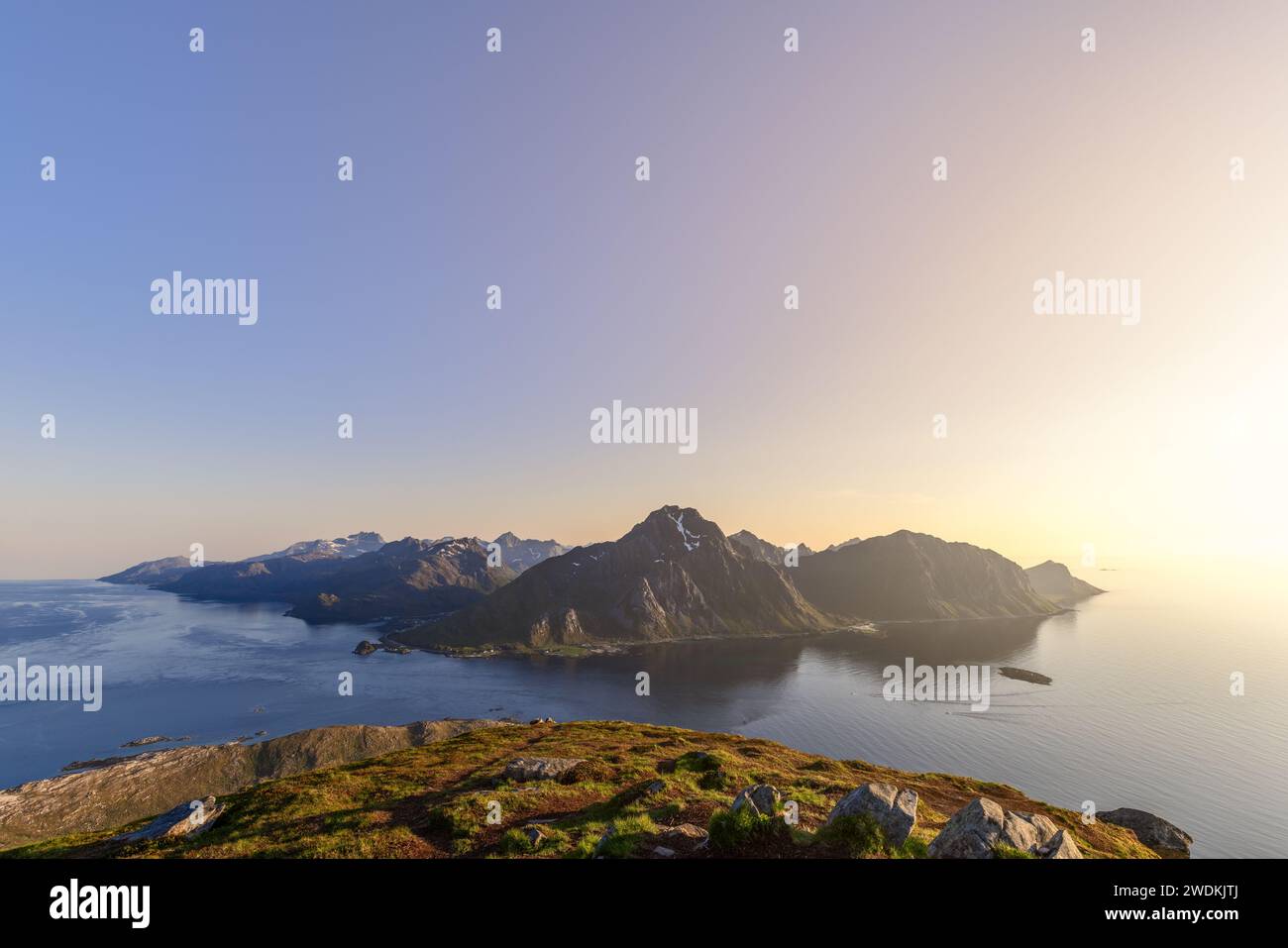 The midnight sun casts a golden glow over the serene landscape of Offersoykammen, overlooking the tranquil Nappstraumen in Lofoten, Norway Stock Photo
