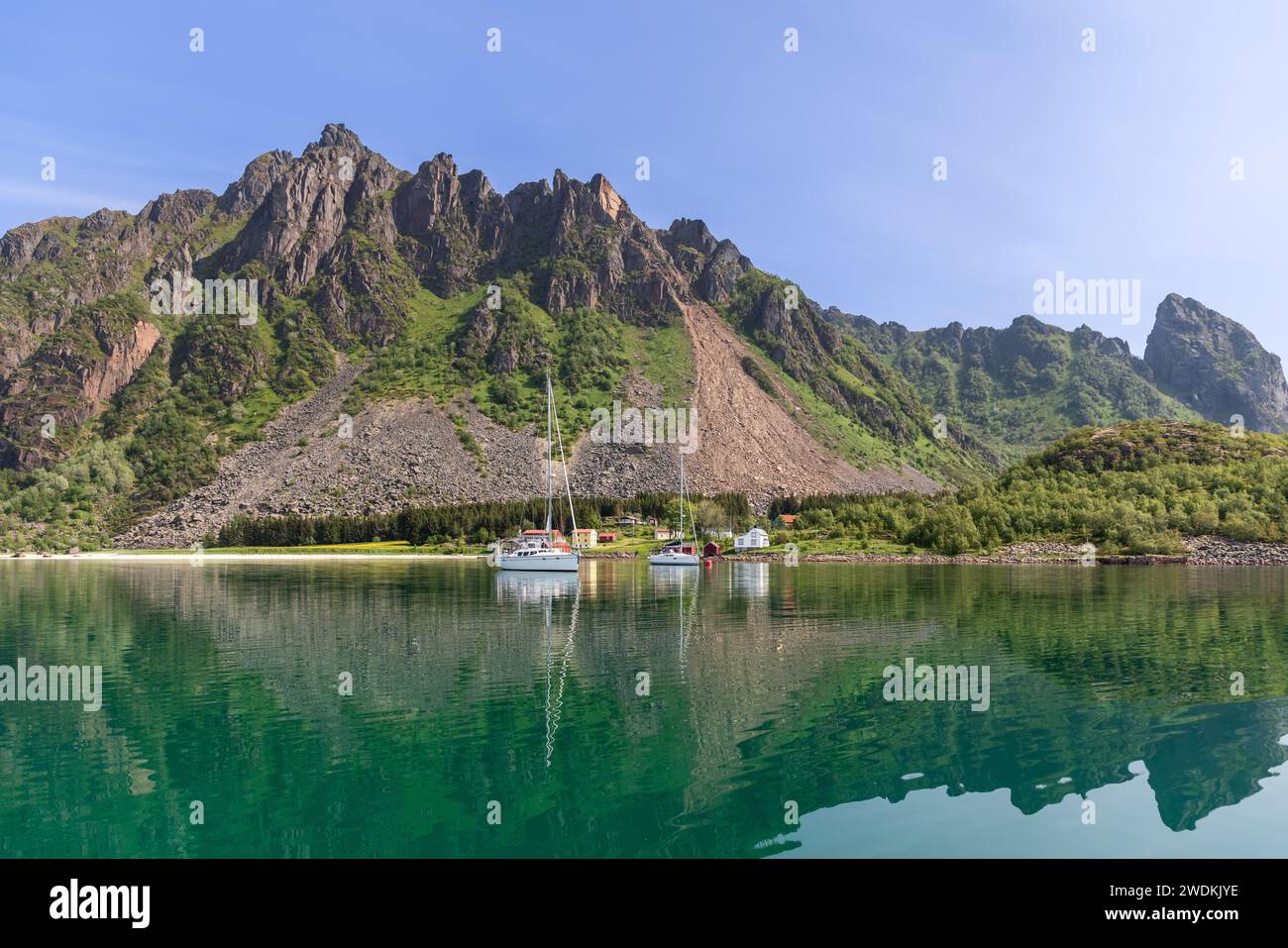 A tranquil summer scene in the Lofoten Islands, where sailboats and traditional Rorbu cabins are mirrored in the still waters Stock Photo