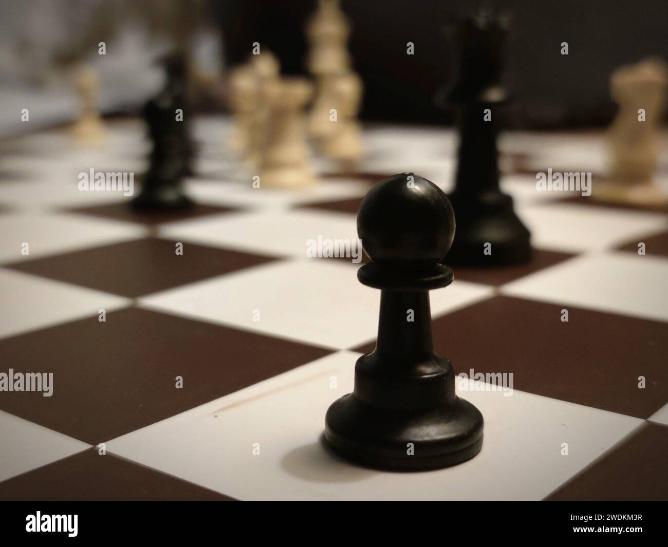 Detailed image of a black pawn on a chess board with other chess pieces in the background. Stock Photo