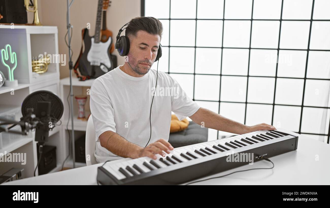 Attractive young hispanic man, a talented musician, immersing himself in the melody, passionately playing the acoustic piano wearing headphones in a l Stock Photo