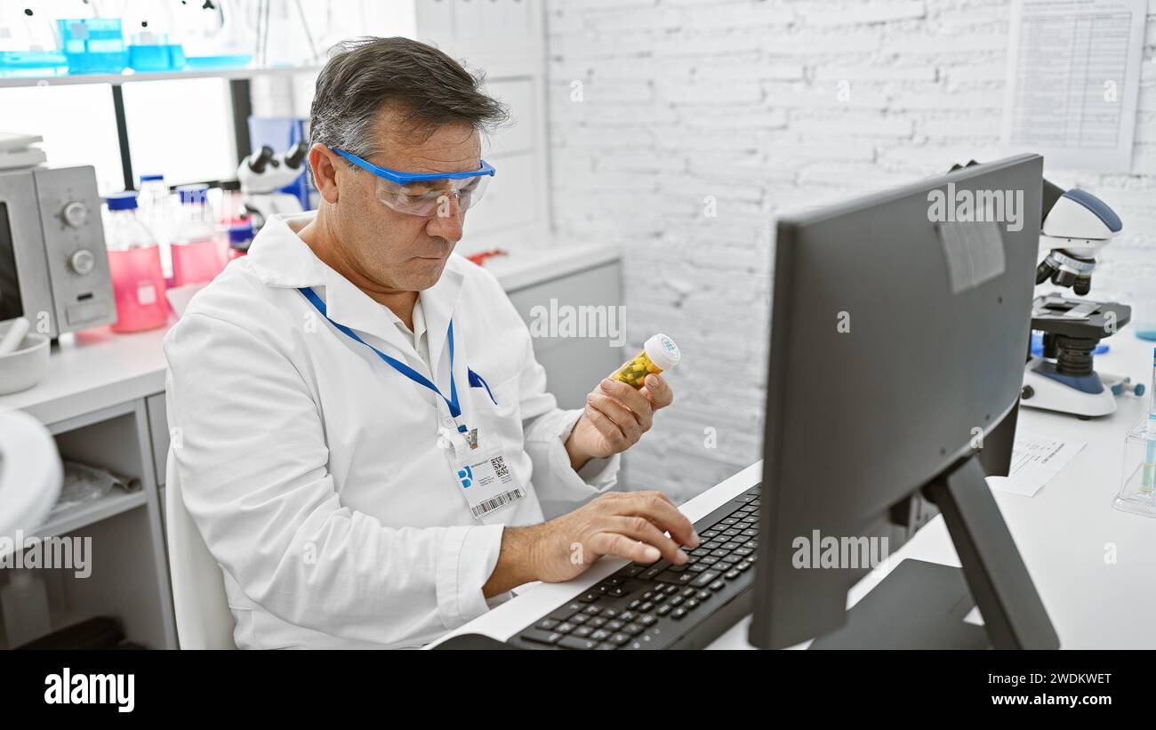Mature man in lab coat examines medication bottle in bright laboratory while using computer. Stock Photo