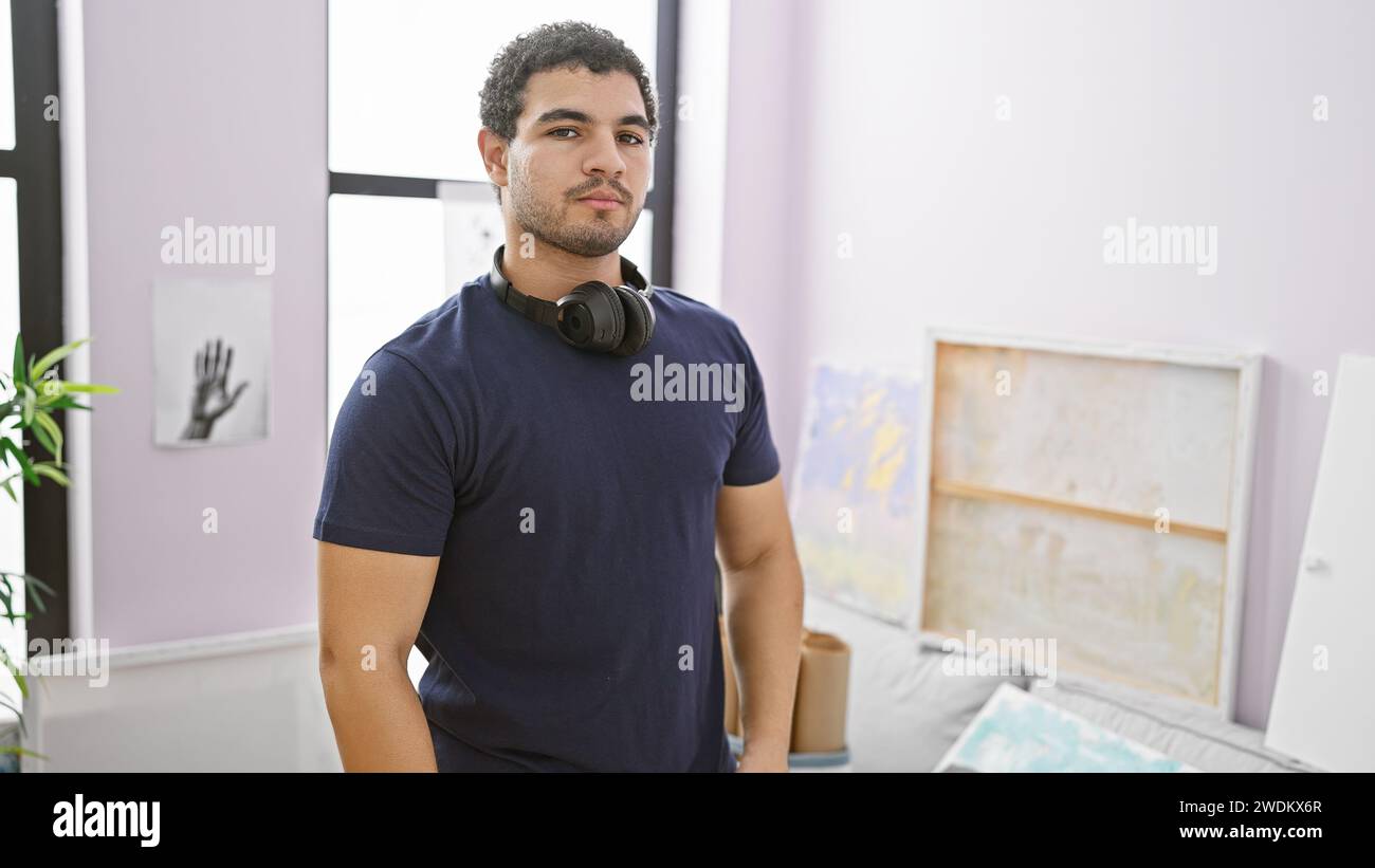 Young man with headphones stands confidently in an indoor artistic studio, embodying creativity and focus. Stock Photo