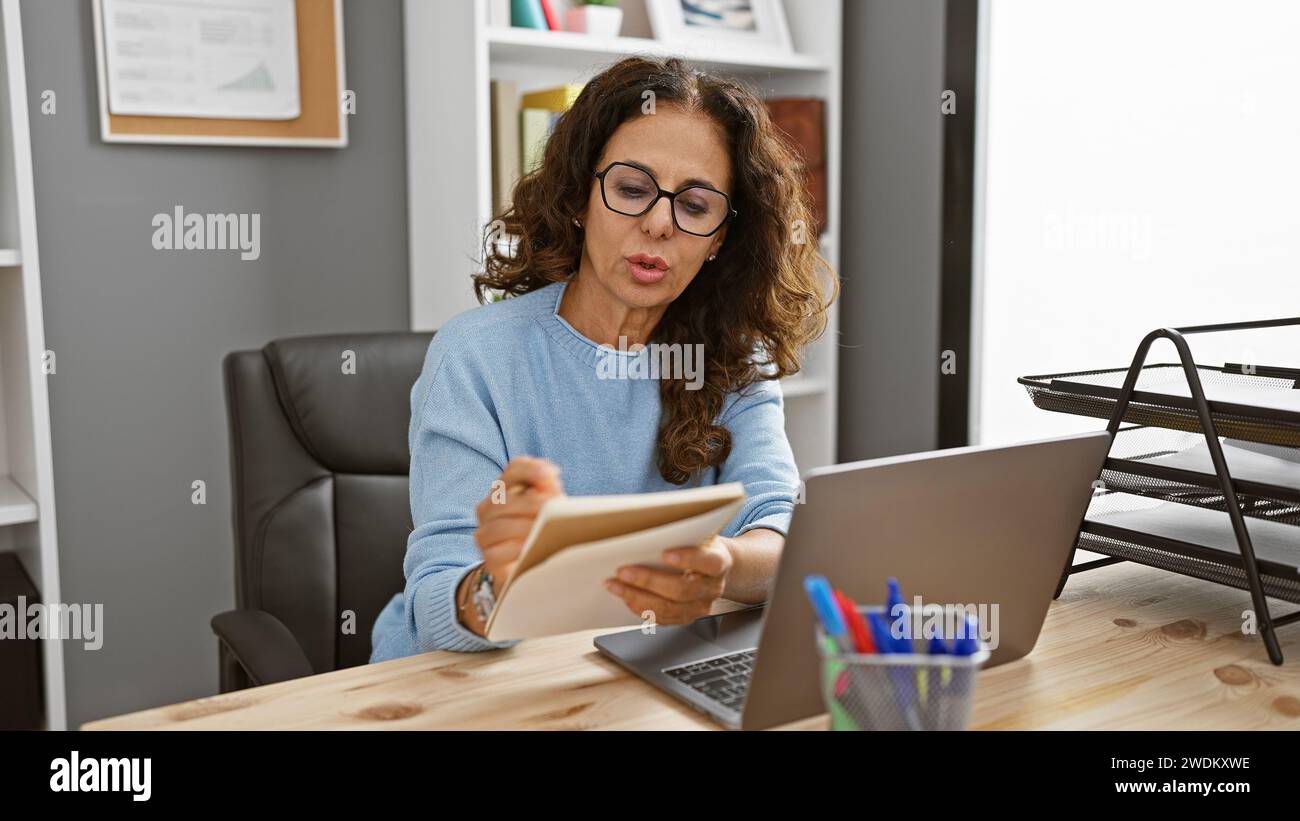 A focused hispanic woman with curly hair works at her laptop in a ...