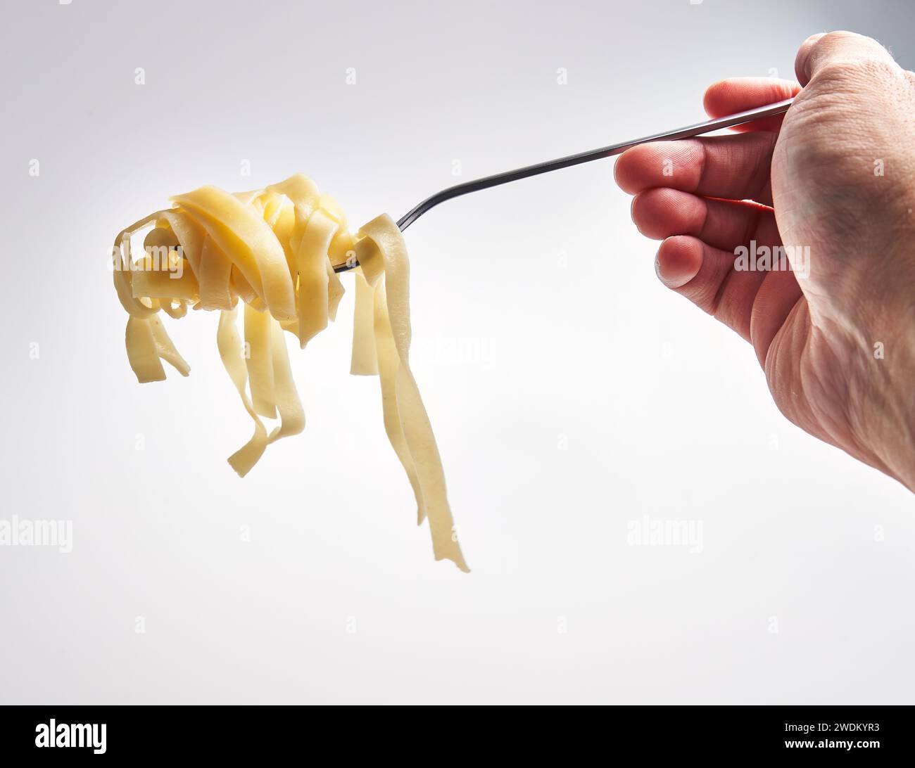 Closeup of a hand twirling fettuccine pasta on a fork against a white