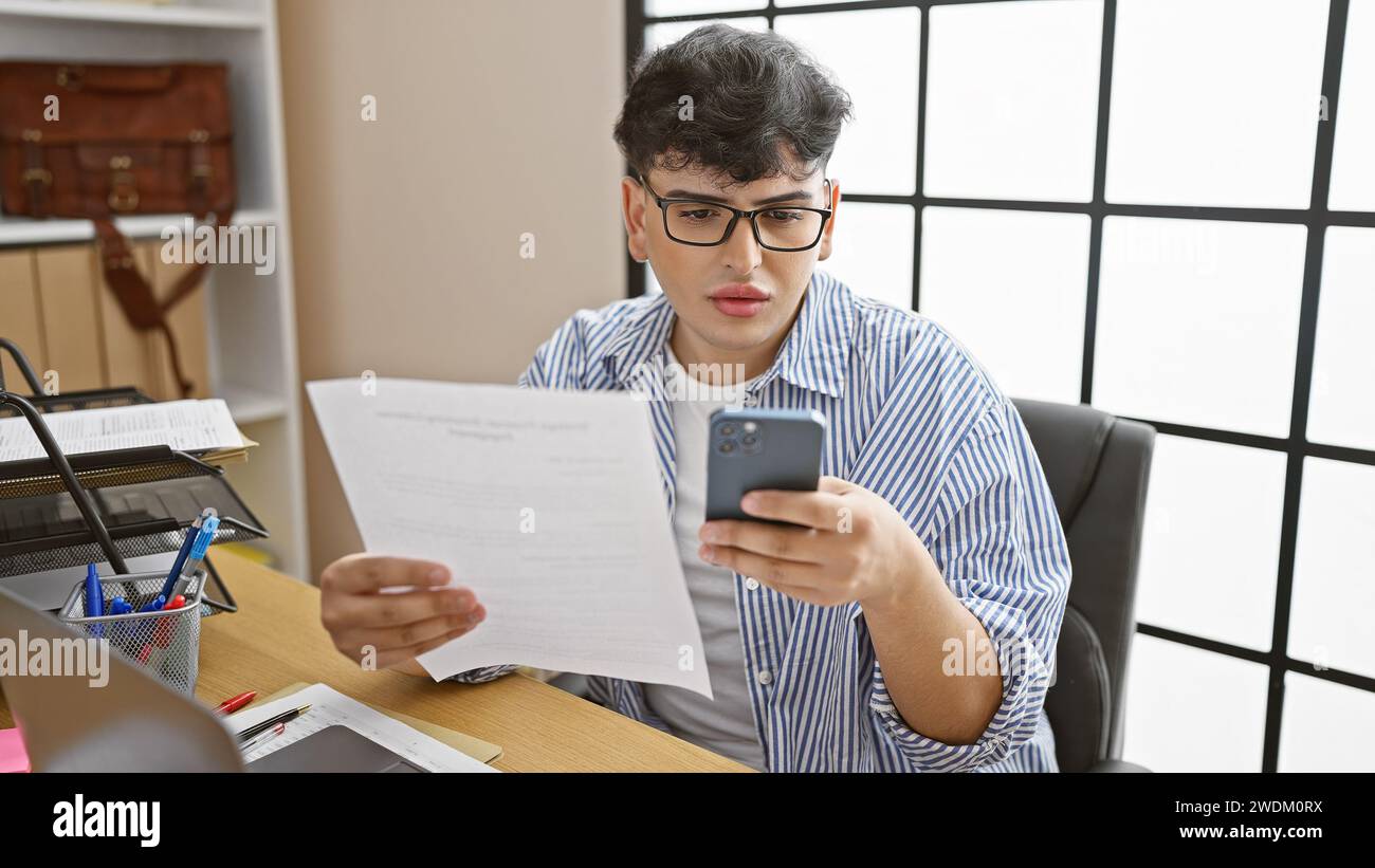 A focused man in an office multitasks with a smartphone and document ...