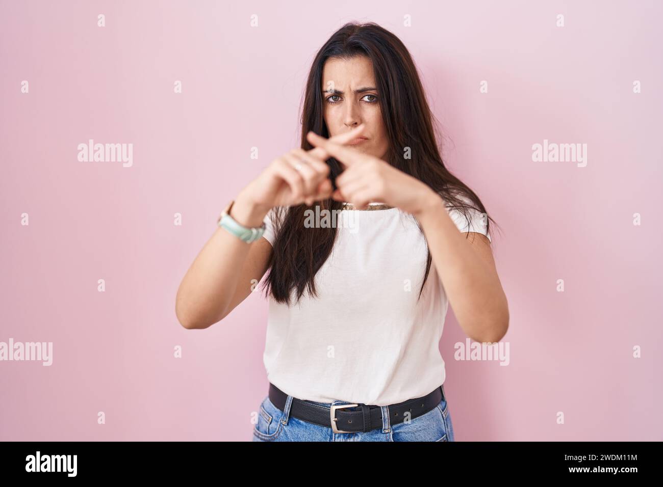 Young brunette woman standing over pink background rejection expression ...