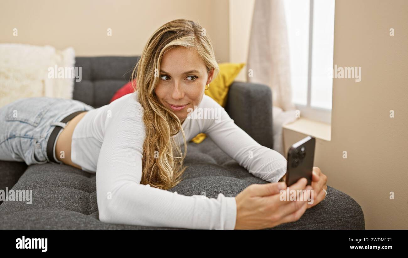 A young, attractive, blonde woman in casual attire takes a selfie on a ...